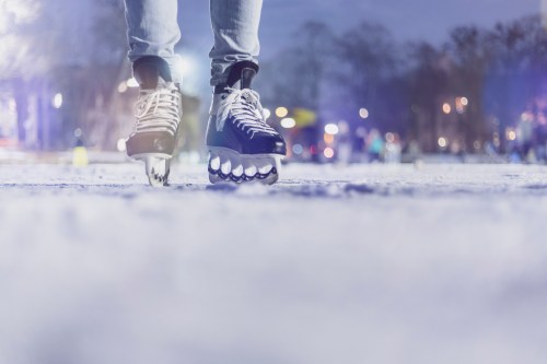 A close-up of a person ice skating on a snowy rink, with blurred skaters and lights in the background.