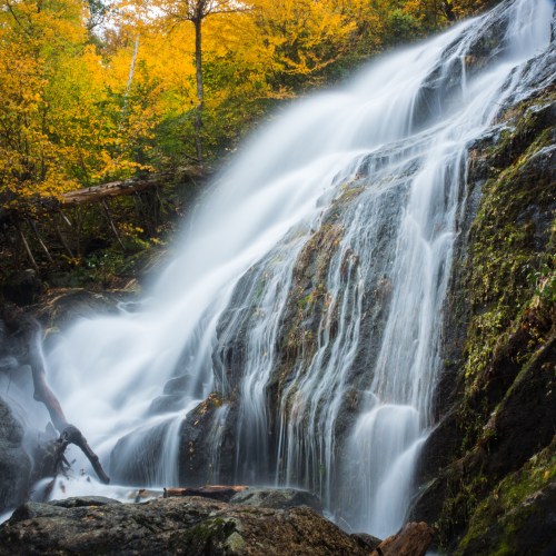 A serene waterfall cascades over rocky terrain, surrounded by vibrant autumn foliage.