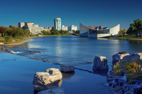 A serene river scene with modern buildings and a unique architectural structure along the water's edge.