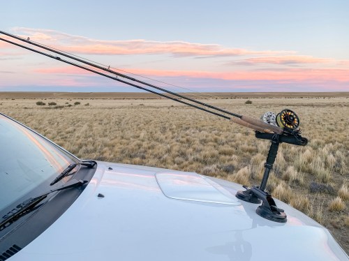 A fishing rod mounted on a vehicle's roof, with a scenic sunset over a grassy landscape in the background.