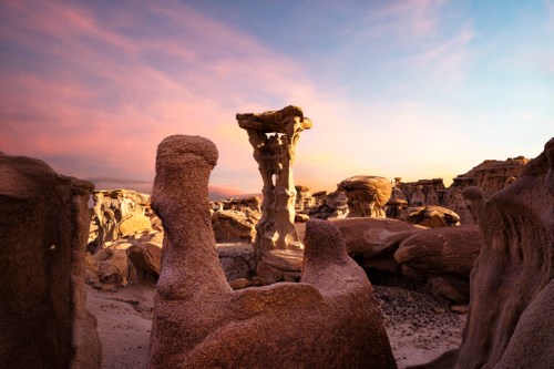 Unique rock formations at sunset, with a towering pillar and textured stone structures under a colorful sky.