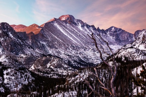 A stunning mountain landscape with snow-covered peaks and a valley, illuminated by a soft sunset glow.