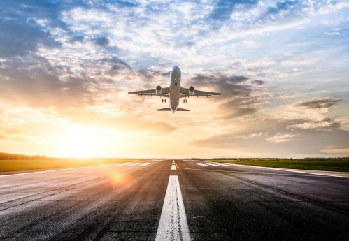 An airplane takes off against a vibrant sunset sky, with a runway visible in the foreground.