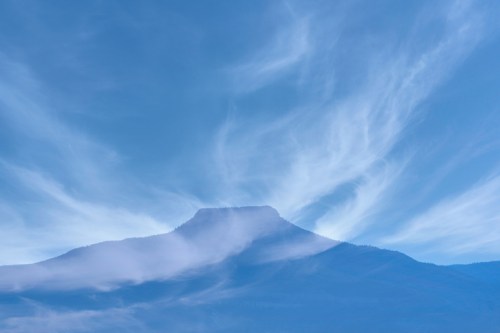 A mountain silhouette under a blue sky with wispy clouds, creating a serene and tranquil atmosphere.