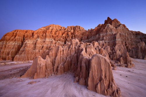 A rugged landscape of colorful rock formations and cliffs under a clear blue sky at dusk.