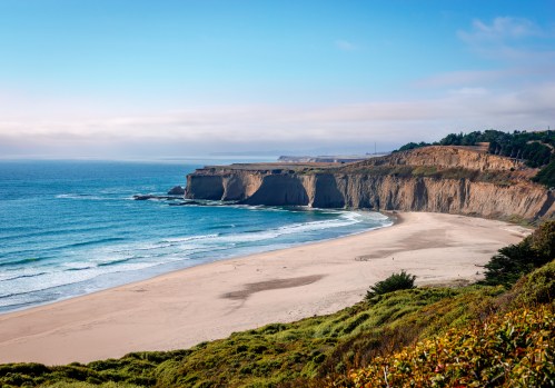A scenic view of a sandy beach with cliffs and gentle waves under a clear blue sky.