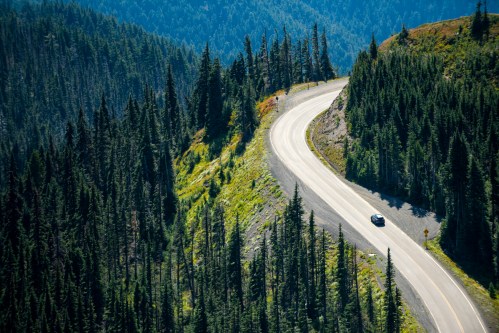 A winding road curves through a lush green forested landscape with mountains in the background.