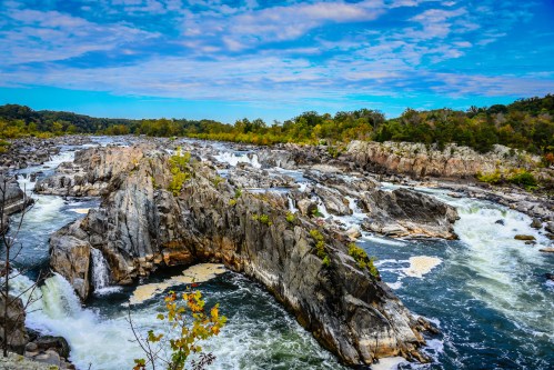 A scenic view of a rocky river landscape with flowing water and lush greenery under a blue sky.