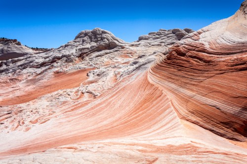 Colorful, layered rock formations with smooth curves under a clear blue sky.