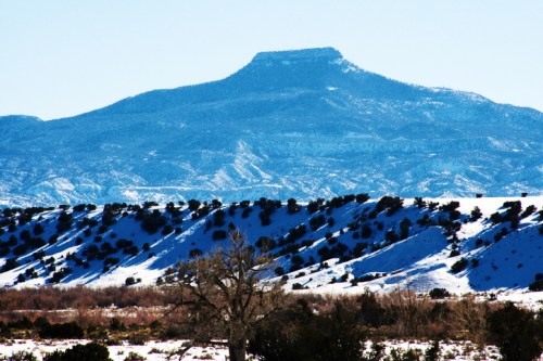 A snow-covered landscape with a prominent mountain peak in the background under a clear blue sky.