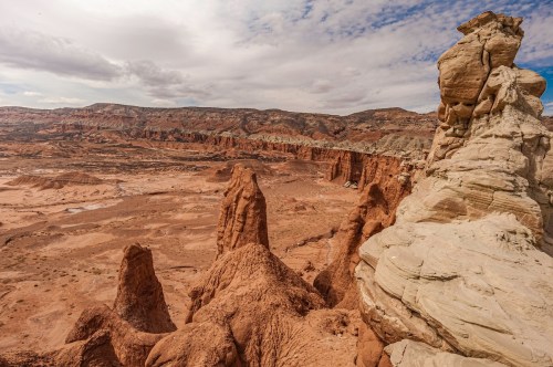 A rugged desert landscape with unique rock formations and layered cliffs under a cloudy sky.