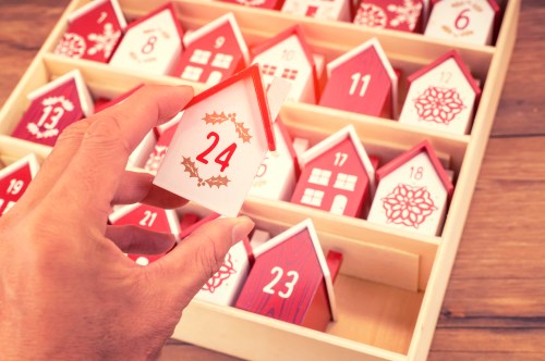 A hand holds a small red and white house marked "24" from an advent calendar with numbered houses.