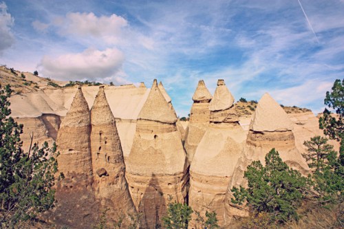 Unique rock formations resembling cones, surrounded by greenery under a blue sky with scattered clouds.