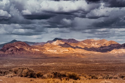 A dramatic desert landscape with rugged mountains under a cloudy sky, showcasing earthy tones and vast open space.