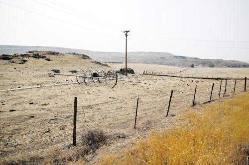A dry, open landscape with a fence, irrigation equipment, and distant hills under a clear sky.