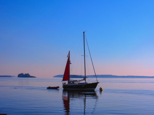 A sailboat with red sails floats on calm waters, with a distant island and blue sky in the background.