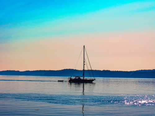 A sailboat glides across calm waters under a blue sky, with distant hills visible on the horizon.