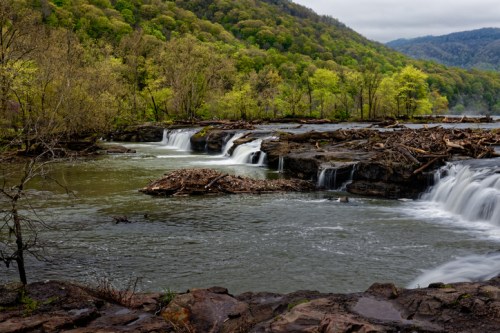 A serene landscape featuring cascading waterfalls surrounded by lush green trees and rocky terrain.