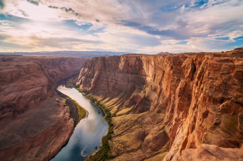 A scenic view of Horseshoe Bend, featuring a winding river surrounded by towering red rock cliffs under a cloudy sky.