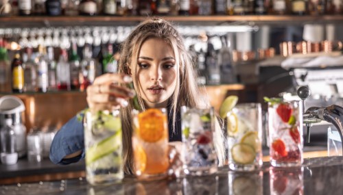 A bartender prepares colorful cocktails with fresh fruits and herbs at a lively bar.