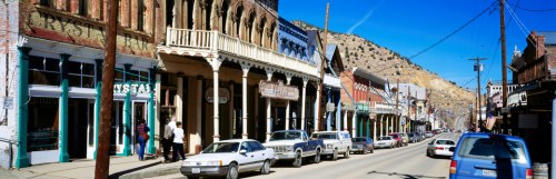 Historic street lined with vintage buildings and parked cars under a clear blue sky. Mountains in the background.