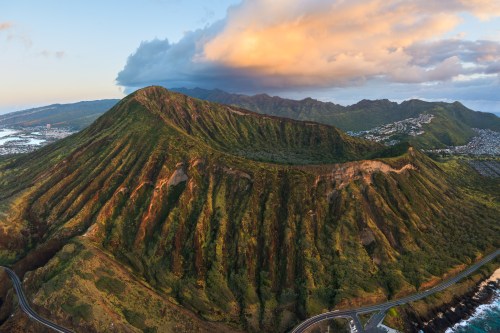 Aerial view of a lush green mountain with ridges, under a colorful sky at sunset.