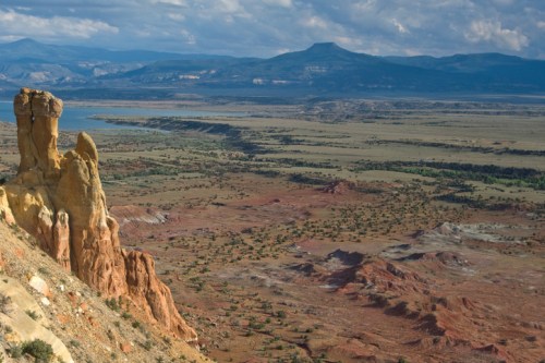 A panoramic view of colorful rock formations and a vast landscape with mountains in the distance under a cloudy sky.