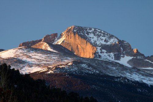 A majestic mountain peak bathed in golden sunlight, surrounded by snow-covered slopes and evergreen forests.