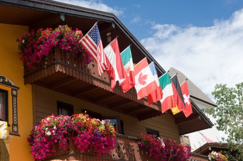 Colorful flower-filled balcony with various national flags displayed against a blue sky.