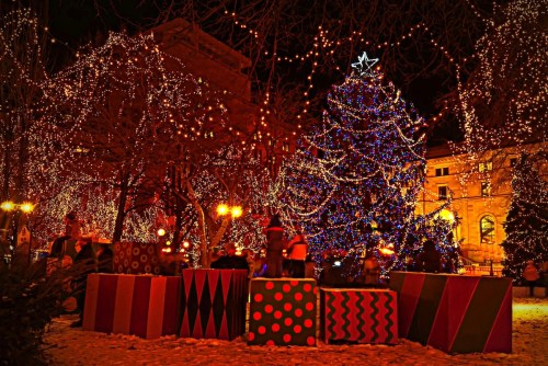 A festive scene featuring a brightly lit Christmas tree surrounded by colorful gift boxes and twinkling lights.