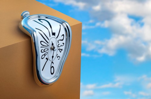 A melting silver clock drapes over a golden cube against a blue sky with clouds, evoking surrealism.