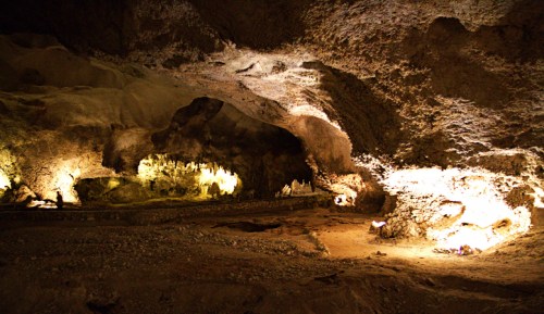 A dimly lit cave interior with rocky formations and illuminated areas, showcasing natural textures and shadows.