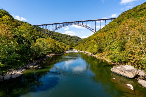 A scenic view of a river surrounded by trees, with a large bridge arching over it under a clear blue sky.