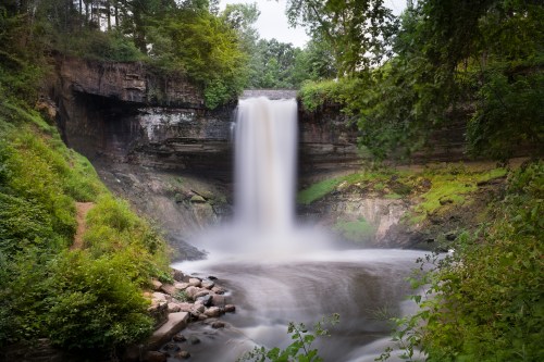 A serene waterfall cascades over rocky cliffs, surrounded by lush greenery and a tranquil river below.