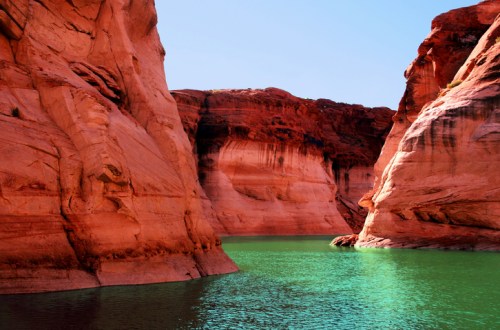 A serene view of red rock formations surrounding a turquoise lake under a clear blue sky.