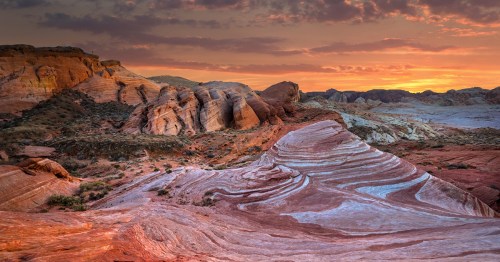 Vibrant desert landscape at sunset, featuring layered rock formations and a colorful sky.