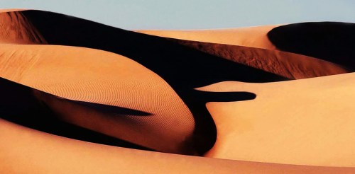 Abstract patterns of sand dunes in warm tones, with contrasting shadows creating a wavy, textured landscape.