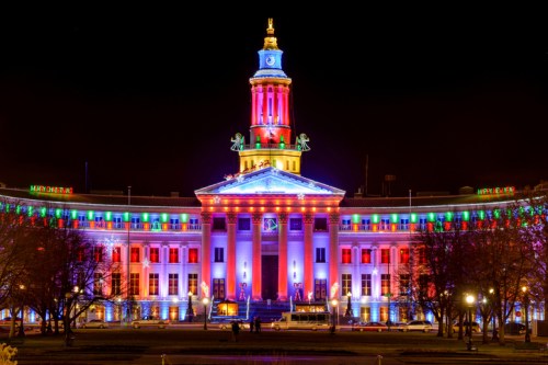 The illuminated Denver City and County Building at night, featuring vibrant red, white, and blue lights.