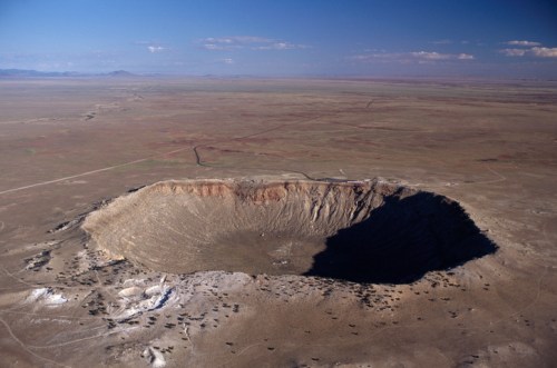 Aerial view of a large, circular crater in a flat, arid landscape under a clear blue sky.