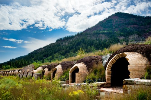 Abandoned brick structures line a grassy hillside, with a mountain and blue sky in the background.