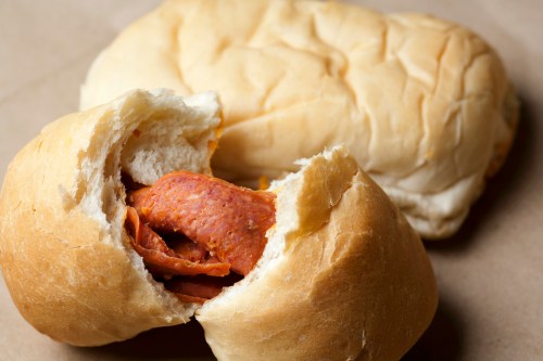 A close-up of a soft bread roll filled with slices of pepperoni, with another roll in the background.
