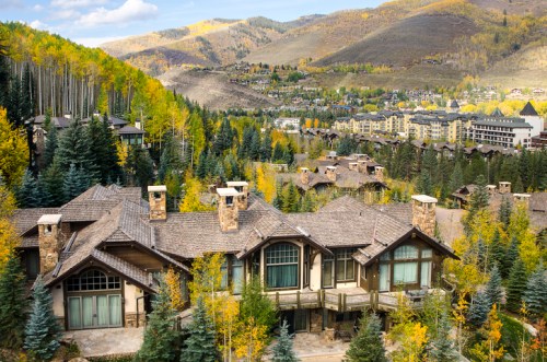 A scenic view of a mountain resort surrounded by autumn foliage and distant buildings in a valley.