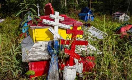 Colorful wooden structures and crosses overgrown with grass in a forested area.