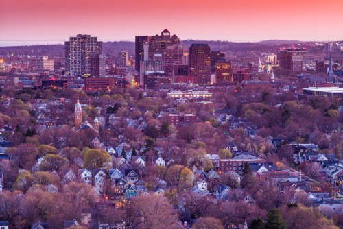 A panoramic view of a city skyline at sunset, with a mix of modern buildings and residential neighborhoods below.
