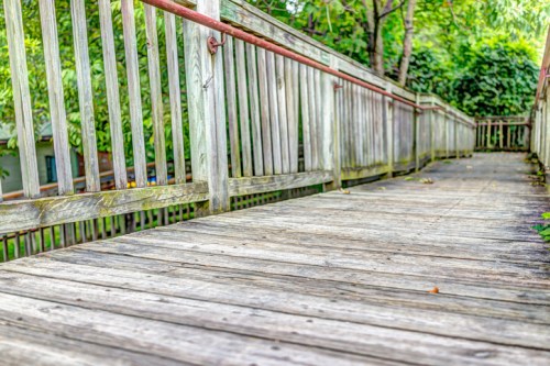 A weathered wooden walkway with a railing, surrounded by greenery and trees.