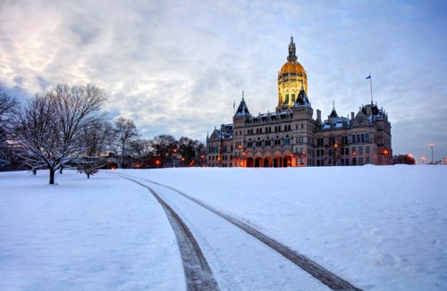 Snow-covered landscape with a historic building and a path leading towards it, under a cloudy sky at dusk.