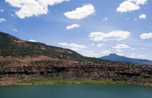 A serene landscape featuring a calm lake, green hills, and a blue sky with fluffy clouds.