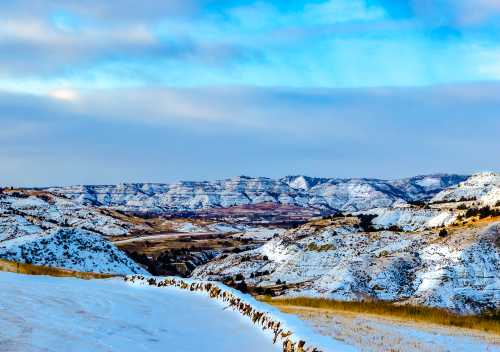 Snow-covered hills and valleys under a blue sky, with a winding road in the foreground.