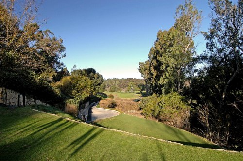 A scenic view of a golf course surrounded by trees and greenery under a clear blue sky.