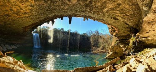 A scenic view of a waterfall cascading into a serene pool, framed by a rocky overhang and lush greenery.